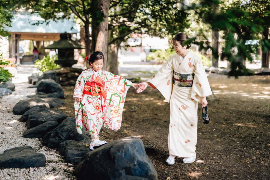 七五三 ロケーション撮影｜神社の境内で母と手をつなぎながら歩く着物姿の女の子